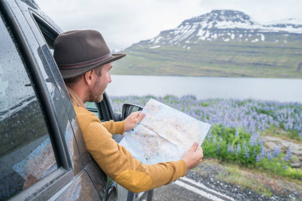 istock Young man in car looking at map, road trip concept vacations 1011556354