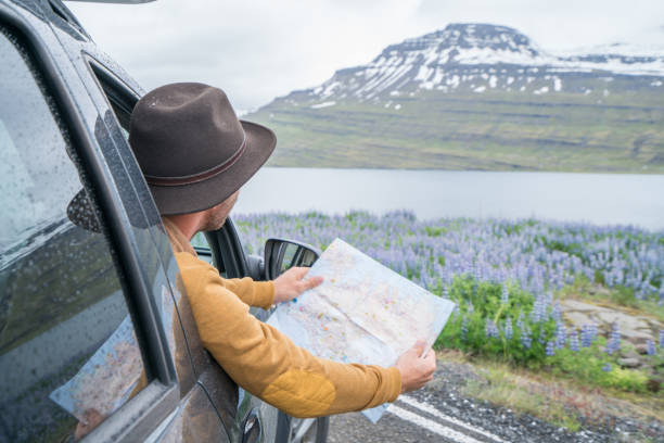 Young man in car looking at map, road trip concept vacations