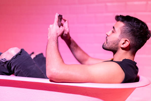 istock Man Using Mobile in the pink bathtube 1011570432