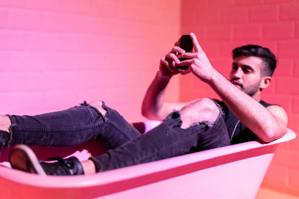 istock Man Using Mobile in the pink bathtube 1011570522