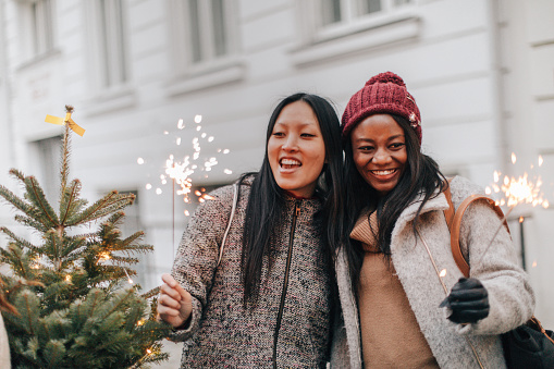 Smiling girlfriends holding sparklers and enjoying in the city during Christmas holidays