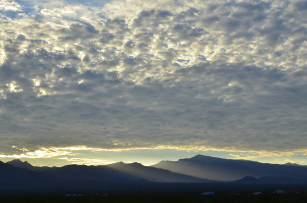 sunrise light rims edge of massive cloud bank over Spring Mountains and the peak of Mount Charleston with misty valleys between in the Mojave Desert town of Pahrump, Nevada, USA