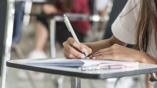 istock Blur school background university students writing answer doing exam in classroom 1011590346