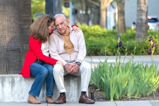 senior Hispanic or middle Eastern man possing with his mature caucasian daughter in the street, she is comforting him