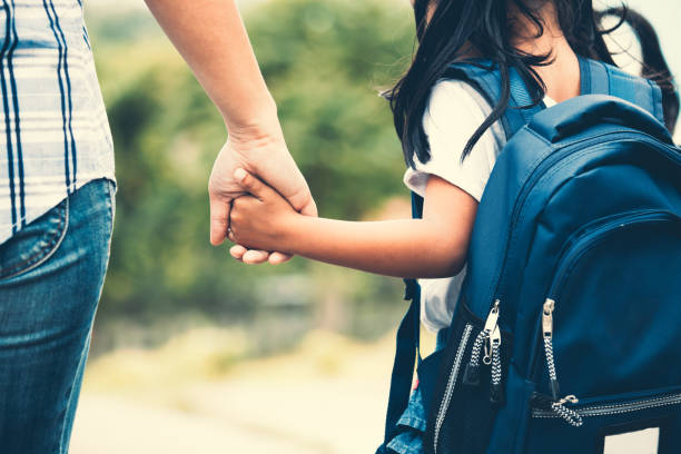 バックパック彼女の母の手を握って、学校に行くとかわいいアジアの瞳の女の子 - parent ストックフォトと画像