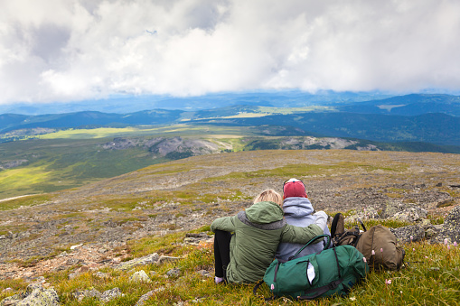 Travel Lifestyle and survival concept rear view.Hiking lovers woman and man with backpack is sitting on the top of the mounting and looking at a beautiful landscape.