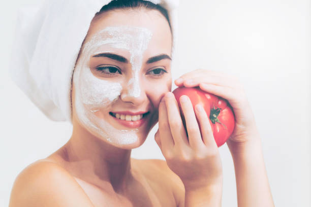 Woman get facial mask with tomato cream extract. Beautiful woman having a facial mask treatment with tomato cream extract showing benefit of nature treatment. Anti-aging cosmetology, facial skin care and luxury lifestyle concept. women facial mask mud cucumber stock pictures, royalty-free photos & images