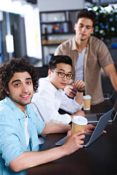 istock three multiethnic businessmen with paper coffee cups sitting at table with laptops at modern office 1011709332