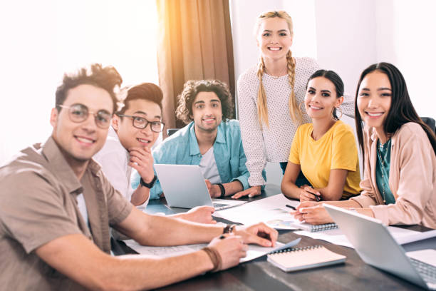 istock group of smiling multicultural business partners sitting at table with laptops and papers during meeting at modern office 1011710108