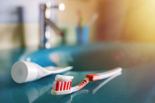 teeth health: brush and toothpaste on blue sink in bathroom. red toothbrush lies in the interior on background of water tap.