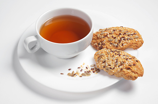 Plate with tea and oatmeal cookies with seeds on white background