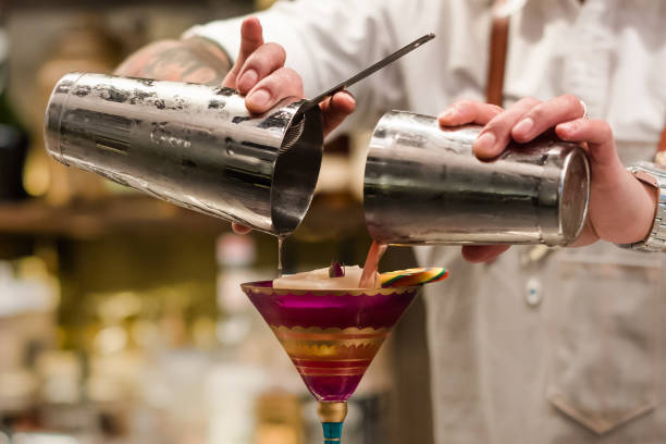 professionelle barkeeper in glas wein aus shaker cocktail gießen. barkeeper in händen cocktail werkzeug halten. mischvorgang alkoholisches getränk. schließen sie herauf bild mit einem teil des menschlichen körpers. - cocktailshaker stock-fotos und bilder