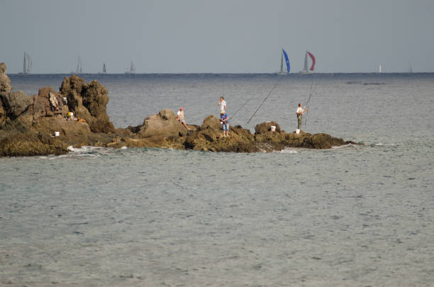 Fishermen and transatlantic race in the background. Risco Verde. Playa de Arinaga. Agüimes. Gran Canaria. Canary Islands. Spain.