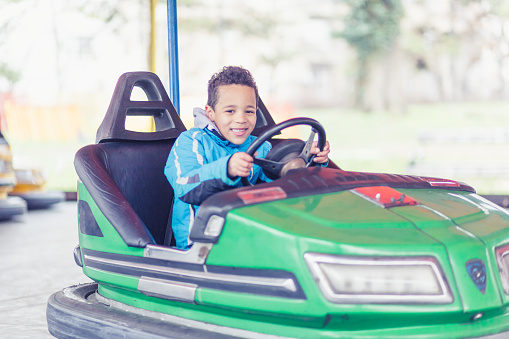 Mixed race boy driving bumper cars in amusement park