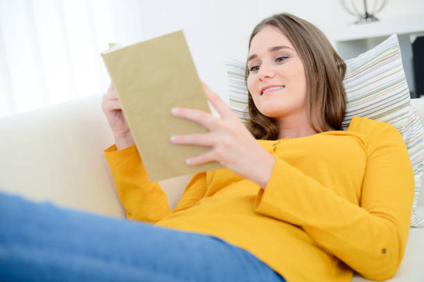 istock cheerful young woman reading a book on sofa at home 1011763364