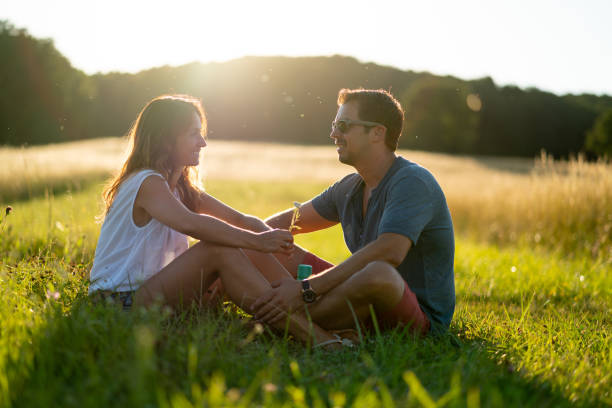 istock smiling couple sitting together in grassland summer sunset 1011782462