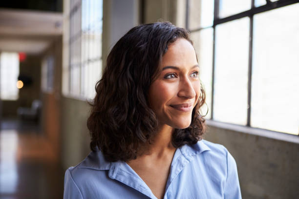 sonriendo a empresaria joven mestiza mirando lejos - business office business person window fotografías e imágenes de stock