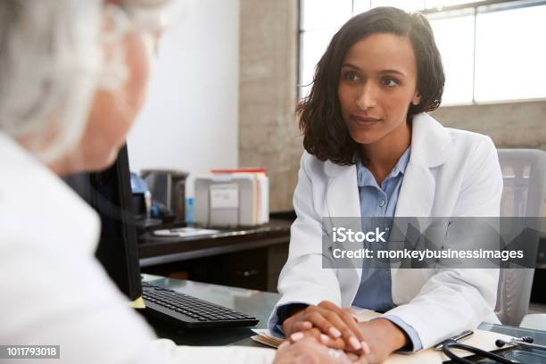 Joven Doctora En Consulta Con El Paciente Mayor Foto de stock y más banco de imágenes de Doctor - Doctor, Paciente, Profesional de salud mental