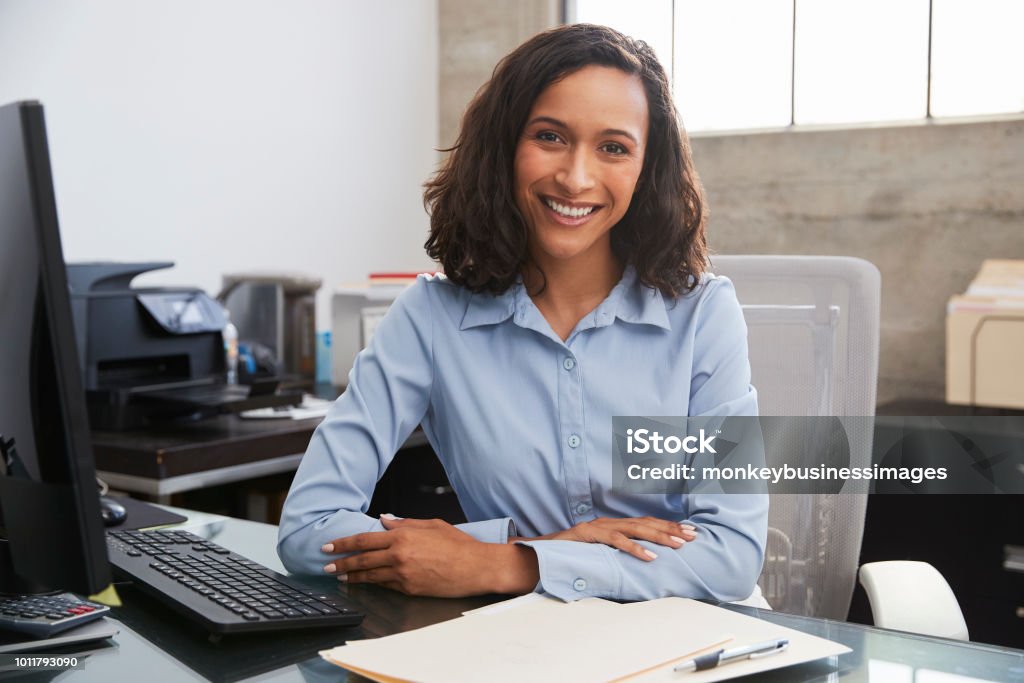 Giovane professionista donna alla scrivania sorridente alla macchina fotografica - Foto stock royalty-free di Donne
