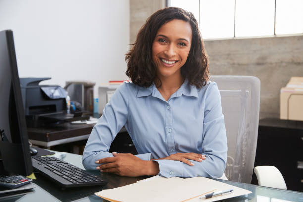 young female professional at desk smiling to camera - clothing well dressed business waist up imagens e fotografias de stock