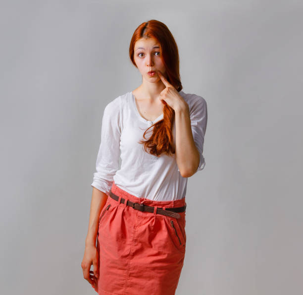istock Feeling and emotions, pretty girl face expression. Fooling around and croaking grimaces, pointing the finger at the face. Casual clothes, copy space, gray background 1011793398