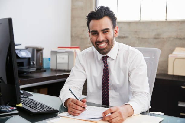 istock Young Hispanic male professional at desk smiling to camera 1011795846
