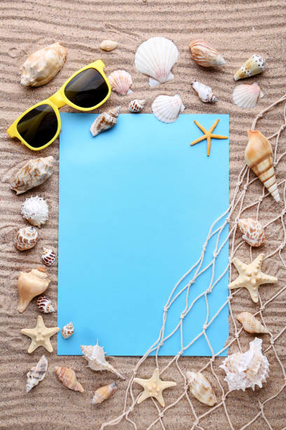 istock Blank sheet of paper with seashells on beach sand 1011813584