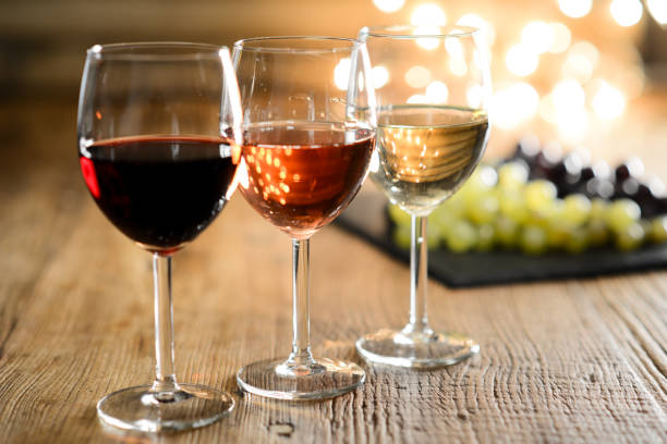 白赤の 3 つのガラスとバラのワインぶどうの背景を持つ木製のレストラン テーブルの中で明かりを - ワイン ストックフォトと画像
