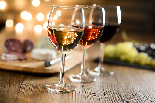 tres copas de vino tinto, vino rosado y vino blanco con queso y delicatessen en mesa de restaurante de madera con tenue luz y acogedor romántico de francés photo