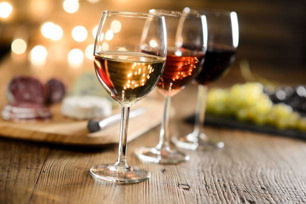 赤ワイン、ロゼと白ワインの 3 つのガラス フランス チーズとロマンチックな薄暗い光と居心地の良い雰囲気の中でのレストランの木製テーブルでデリカテッセン - 地下貯蔵室 写真 ストックフォトと画像