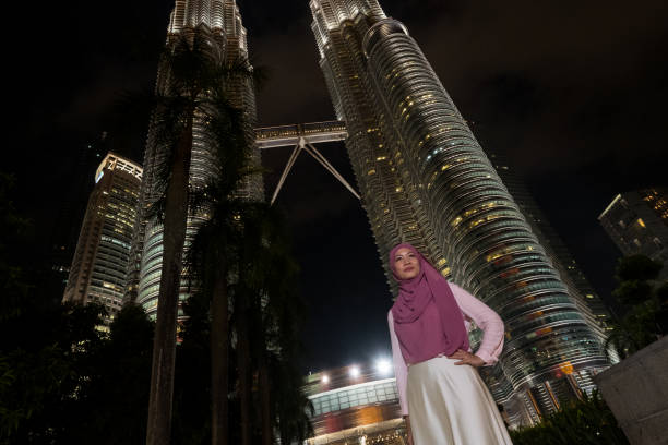 A natural portrait of a beautiful young Malaysian Business woman wearing her hijab and with eyeglasses standing in front of the Petronas Towers