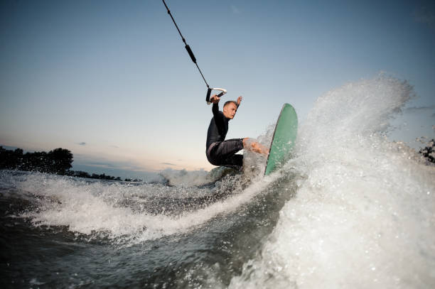 активный вейксерфер, ехая по синей реке высокими волнами с брызгами - wakeboarding waterskiing water ski sunset стоковые фото и изображения
