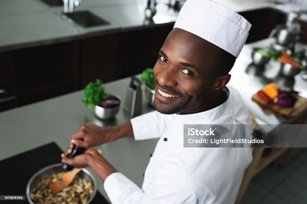Smiling African american cook seasoning dish by kitchen stove Chef Stock Photo