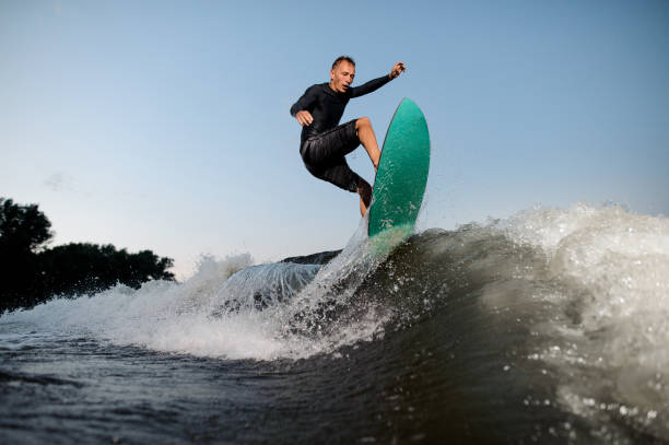активный и молодой серфер после прыжков на доске для пробуждения вниз по реке - wakeboarding waterskiing water ski sunset стоковые фото и изображения
