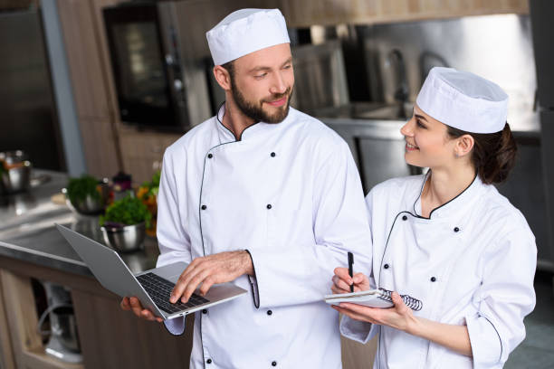 istock chefs using laptop at restaurant kitchen and looking at each other 1011819686