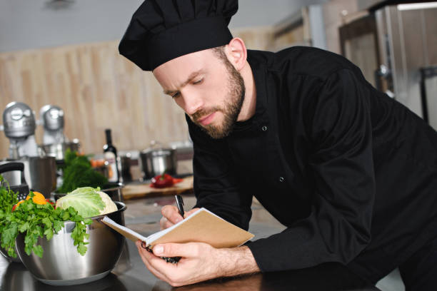 istock side view of handsome chef writing down new recipe to notebook at restaurant kitchen 1011819854