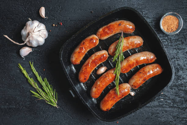 istock Top view on fried sausages in a black frying pan on a black stone table 1011834824