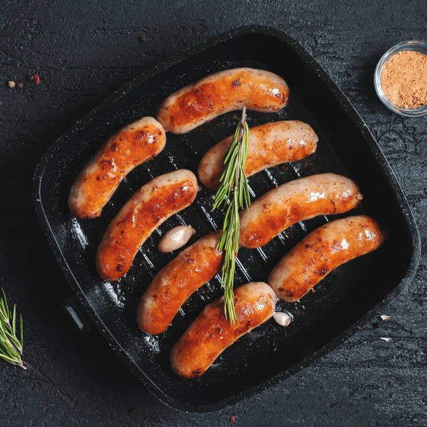 istock Top view on fried sausages in a black frying pan on a black stone table 1011834828