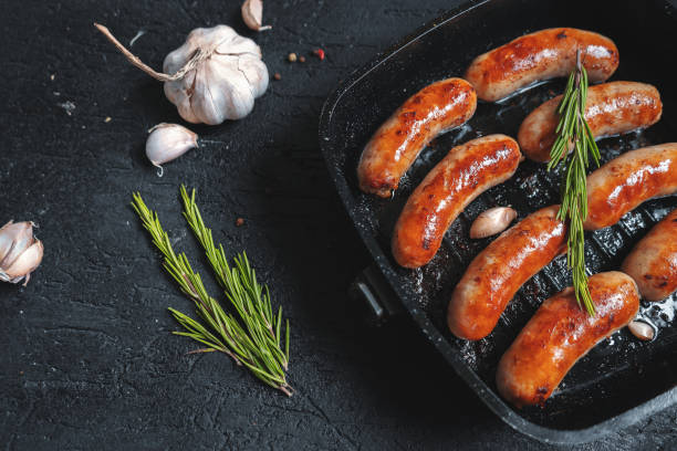 istock Top view on fried sausages in a black frying pan on a black stone table 1011834912