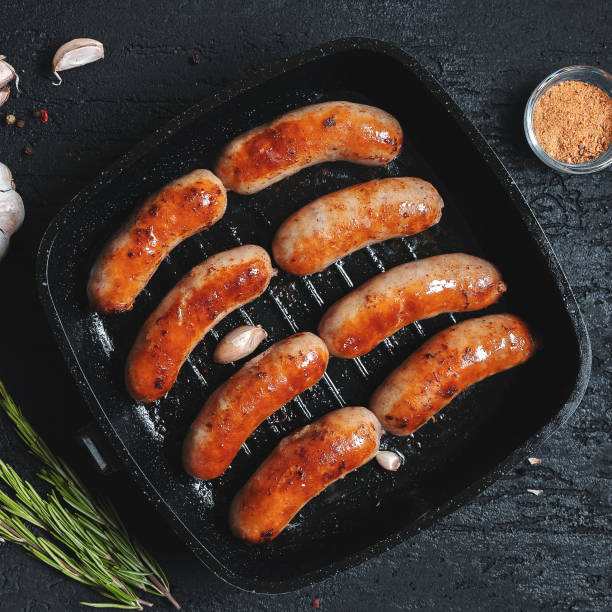 istock Top view on fried sausages in a black frying pan on a black stone table 1011834926