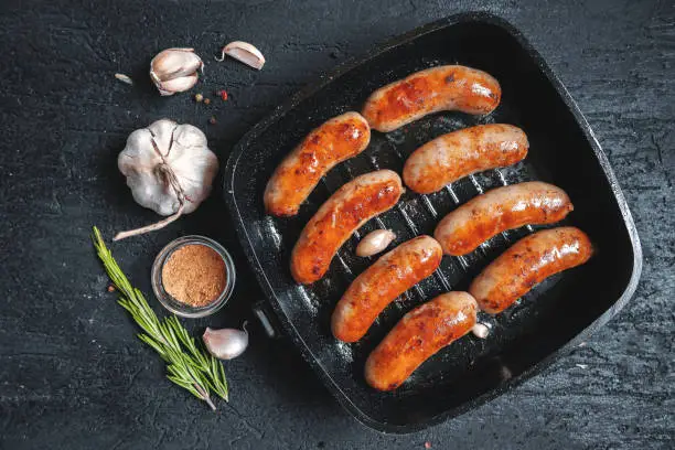 Photo of Top view on fried sausages in a black frying pan on a black stone table