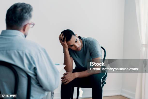 Depressed Teenager Looking Away While Talking To His Therapist Stock Photo - Download Image Now