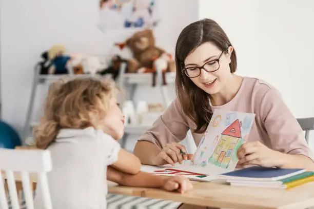 Photo of A professional child education therapist having a meeting with a kid in a family support center.