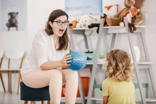 um jogo sensorial com uma bola azul, interpretado por uma terapeuta profissional de criança com um garoto em um centro de apoio à família. - behavioral problems - fotografias e filmes do acervo