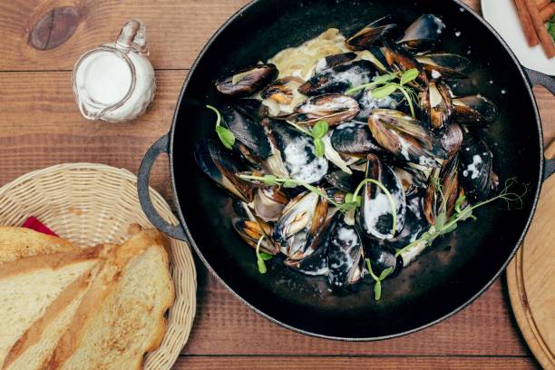 mussels in white cream sauce with bread and herbs at wooden background