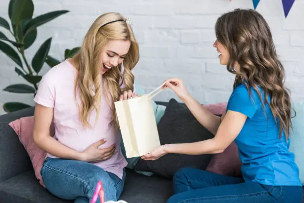 side view of woman presenting gift to pregnant friend at baby-party