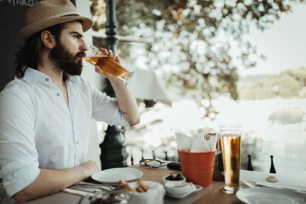 Bearded man drinking beer in a restaurant and enjoying the view from a balcony