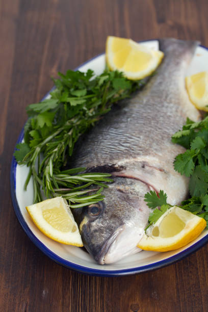 istock raw fish with herbs and lemon on dish on wooden background 1011911504