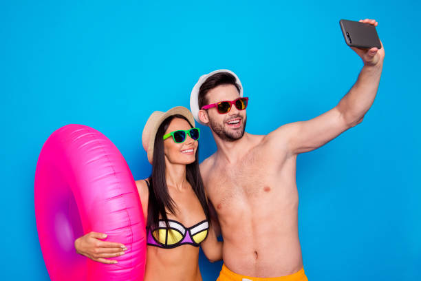 концепция летнего отдыха и медового месяца. парень и девушка, одетые в пляжную одежду, делают селфи на смартфоне с надувным жизненным кольц� - personal flotation device стоковые фото и изображения