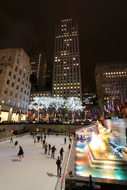Rockefeller Center Skating Rink in Manhattan, New York City Manhattan, New York City, USA, November 1st, 2014. Night shot showing the Rockefeller Center Skating Rink, the in vibrant colors illuminated fountain and the surrounding skyscrapers. Few people skating on the ice. rockefeller ice rink stock pictures, royalty-free photos & images